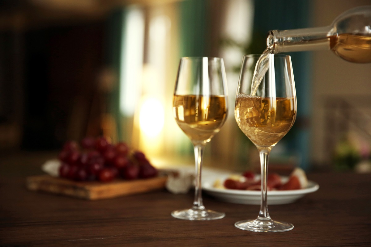 Dwa kieliszki wina do których wlewane jest białe wino
